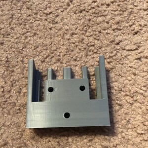 May include: A gray 3D printed plastic part with four slots and three holes.