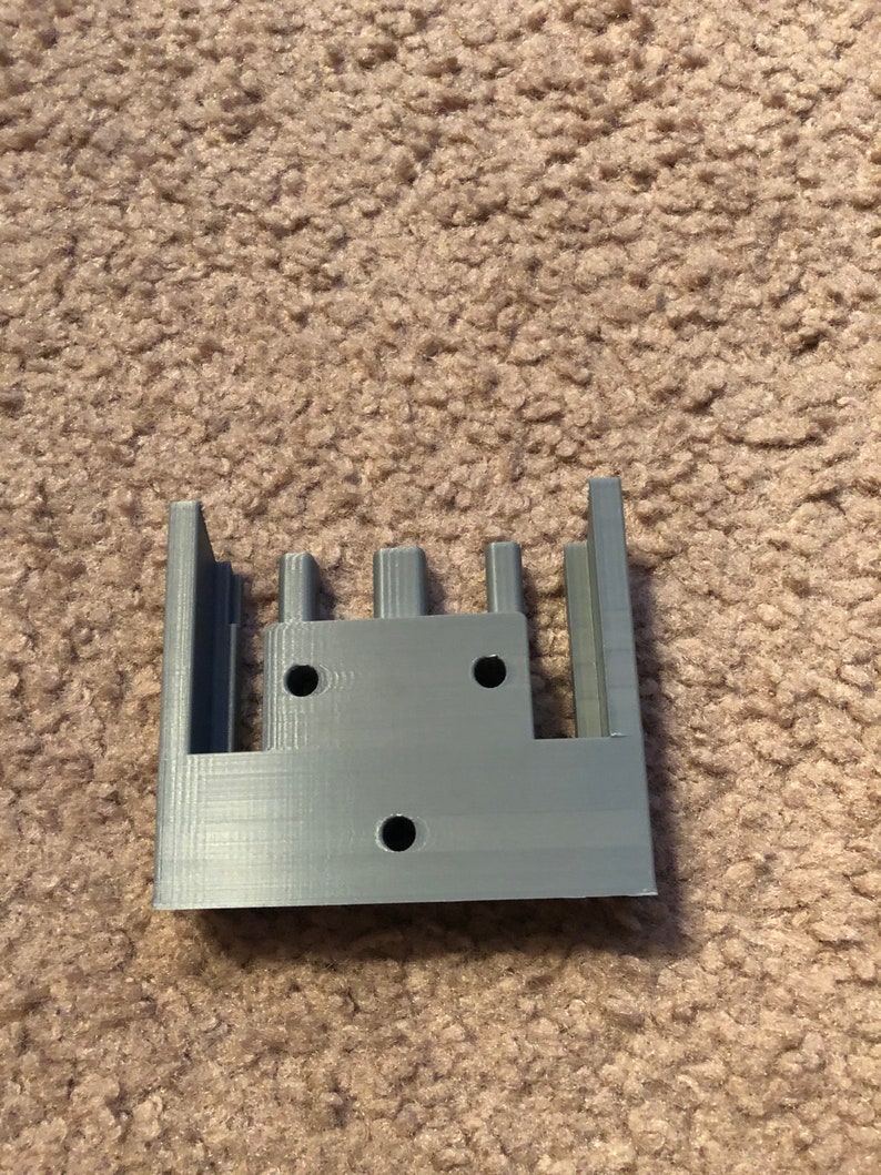 May include: A gray 3D printed plastic part with four slots and three holes.