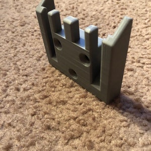 May include: A gray 3D printed plastic wall mount with multiple slots and holes.