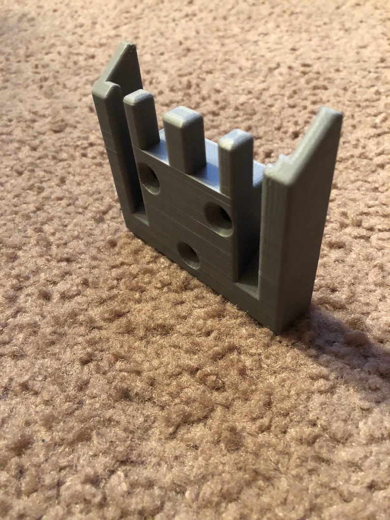 May include: A gray 3D printed plastic wall mount with multiple slots and holes.