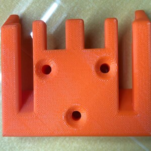 May include: Orange plastic 3D printed object with four slots and three holes.