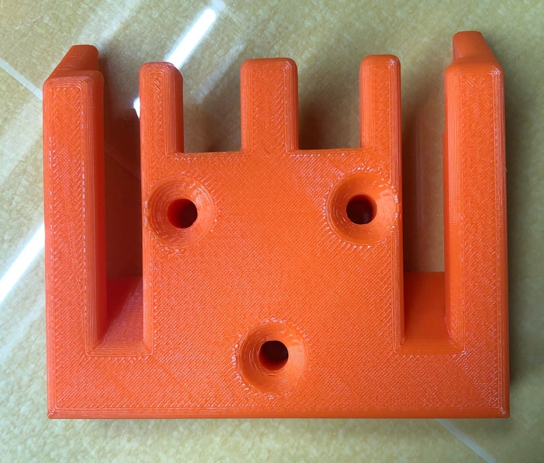 May include: Orange plastic 3D printed object with four slots and three holes.