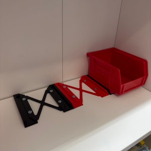 May include: A red plastic storage bin with a black metal shelf support system. The bin is sitting on a white shelf.