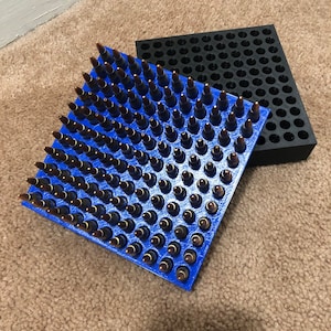 May include: A blue plastic ammo storage tray with rows of brown bullets. The tray is filled with bullets and is sitting on a brown carpet.