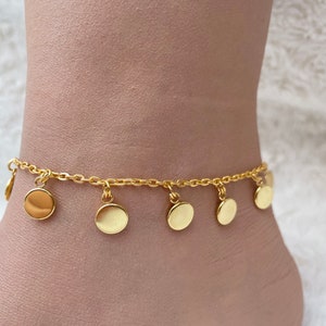 Puede incluir: Tobillera dorada con una cadena delicada y múltiples dijes redondos. Los dijes están espaciados uniformemente y cuelgan de la cadena.