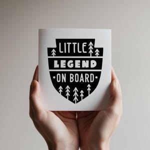 May include: A white card with black text and a black and white graphic of a shield with trees. The text reads "Little Legend On Board".