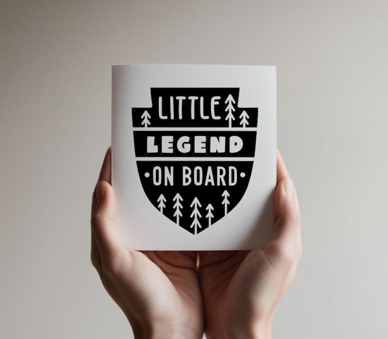 May include: A white card with black text and a black and white graphic of a shield with trees. The text reads "Little Legend On Board".