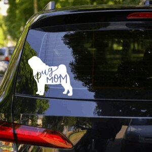 May include: A white car with a black rear window. The rear window has a white vinyl sticker of a pug dog with the text "Pug Mom" underneath.