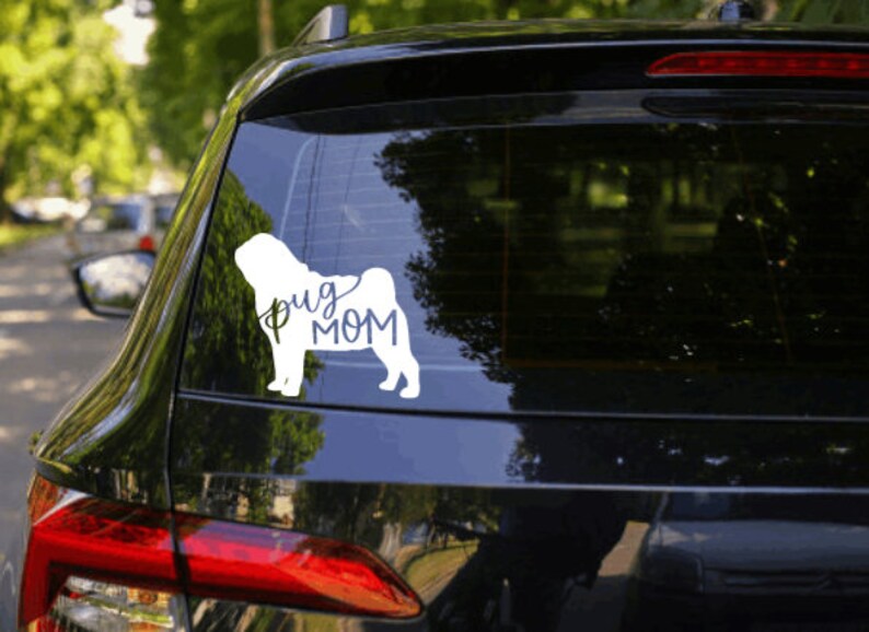 May include: A white car with a black rear window. The rear window has a white vinyl sticker of a pug dog with the text "Pug Mom" underneath.
