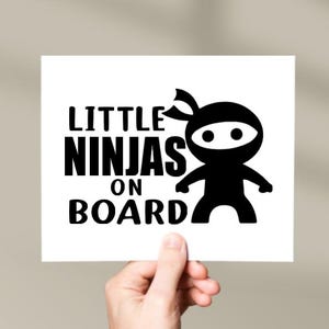 Puede incluir: Tarjeta blanca con texto negro que dice "Little Ninjas on Board" y una silueta negra de un ninja con m&aacute;scara.