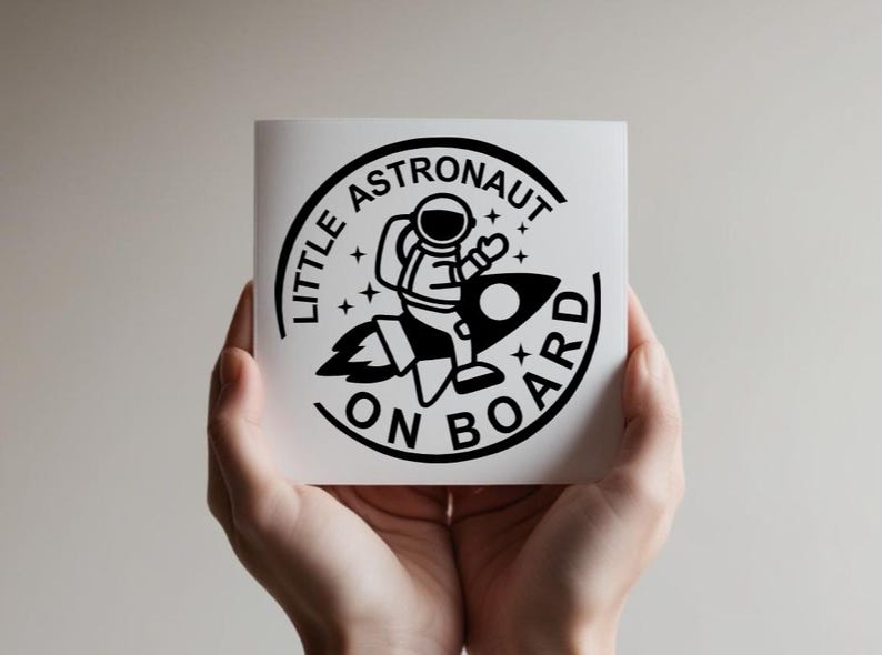 May include: A square white decal featuring a black circular graphic of an astronaut riding a rocket ship. The text LITTLE ASTRONAUT ON BOARD is printed in a bold black sans-serif font along the circular border, accented by small star icons.