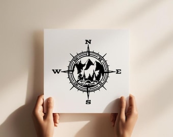 May include: A square white sign featuring a black graphic of a compass rose. The center of the compass contains a silhouette illustration of mountain peaks, a dense forest of pine trees, and stylized ocean waves. The cardinal directions N, S, E, W are clearly marked in bold black lettering.