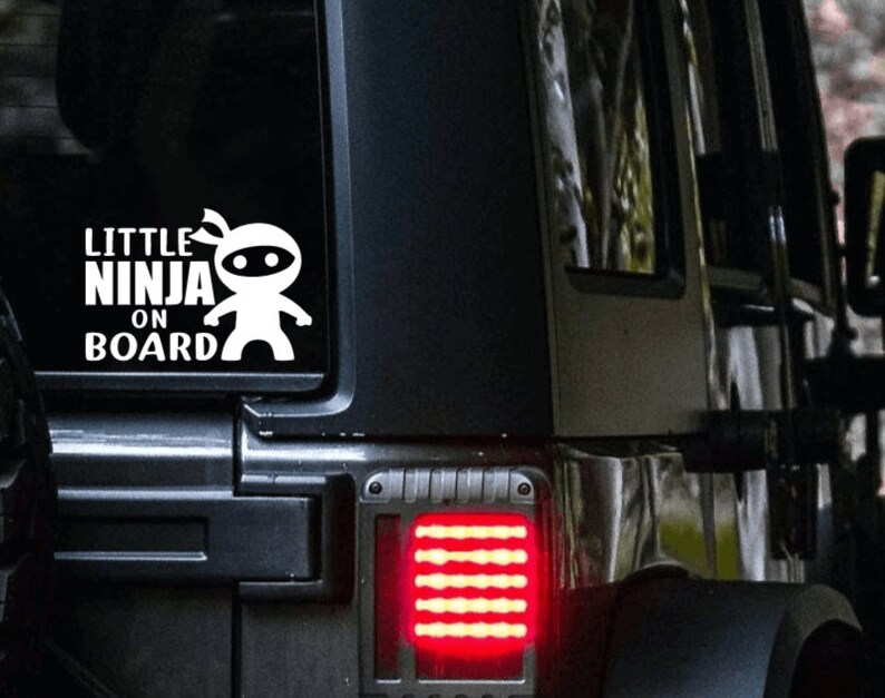 Puede incluir: Calcoman&iacute;a de vinilo blanco con el texto "Little Ninja On Board" y un ninja de dibujos animados con una m&aacute;scara negra. La calcoman&iacute;a est&aacute; en la ventana trasera de un Jeep negro.