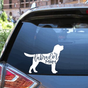 Pu&ograve; includere: Silhouette bianca di un Labrador Retriever con il testo "Labrador Mom" su un finestrino di un'auto.