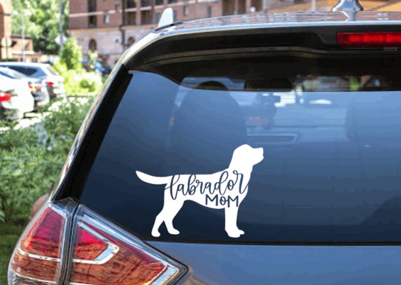 Pu&ograve; includere: Silhouette bianca di un Labrador Retriever con il testo "Labrador Mom" su un finestrino di un'auto.