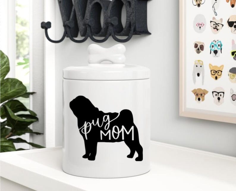 May include: White ceramic jar with a bone-shaped lid. The jar has a black silhouette of a pug with the text "pug mom" printed on it.