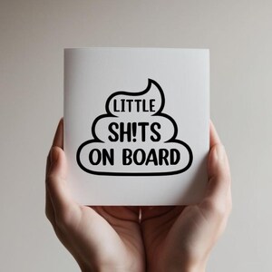 May include: A square white card featuring a black graphic of a stylised poop emoji. The text printed in black capital letters inside the graphic reads LITTLE SH!TS ON BOARD. The design is centred on the card with a clean and bold sans-serif font.