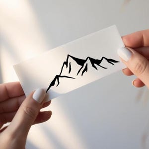 Puede incluir: Una pegatina rectangular blanca que presenta una ilustración minimalista de líneas negras de una cordillera. El diseño consiste en picos afilados y angulosos y laderas irregulares representadas en un estilo de tinta negra continua sobre fondo blanco.