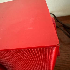 Puede incluir: Una radio vintage roja con una rejilla de altavoz y un cable.