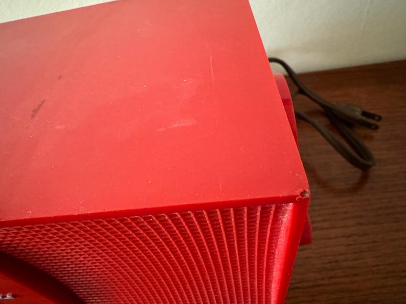 Puede incluir: Una radio vintage roja con una rejilla de altavoz y un cable.