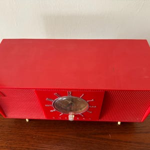 Puede incluir: Un radio despertador vintage rojo con una cara cromada y un patr&oacute;n de rejilla en la parte delantera.
