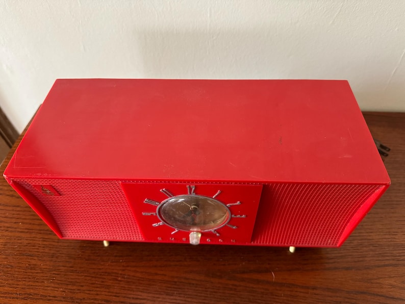 Puede incluir: Un radio despertador vintage rojo con una cara cromada y un patr&oacute;n de rejilla en la parte delantera.