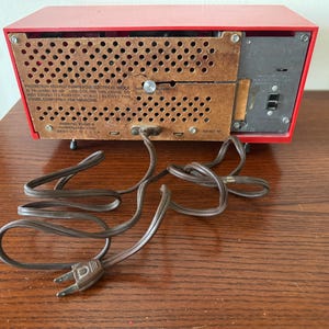 Puede incluir: Radio vintage rojo AM/FM con un cable marr&oacute;n y un cable de alimentaci&oacute;n negro. La parte posterior de la radio tiene una etiqueta que dice "ADVERTENCIA: PELIGRO DE DESCARGA EL&Eacute;CTRICA DE ALTA TENSI&Oacute;N. EN CASO DE DUDA, CONSULTE LAS INSTRUCCIONES CORRECTAS. NO ABRIR. SI EL CABLE DE ALIMENTACI&Oacute;N EST&Aacute; DA&Ntilde;ADO, RETIRE ESTE CABLE COMPLETAMENTE PARA LAS REPARACIONES."