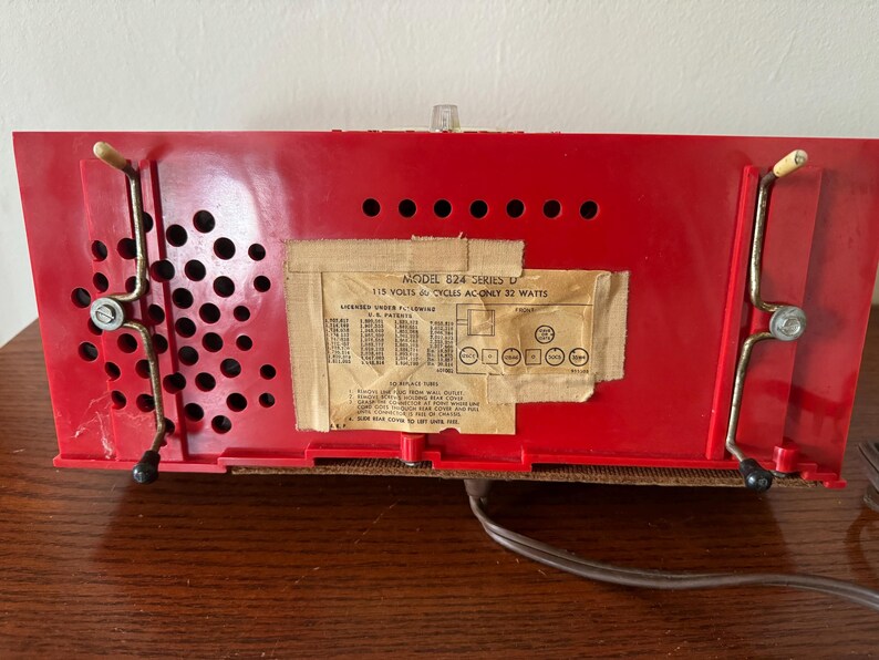 Puede incluir: Radio vintage roja con una etiqueta en blanco y negro que dice "Modelo 824 Serie II 115 Voltios 60 Ciclos AC Solo 32 Vatios".