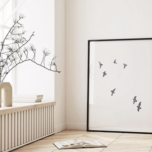 May include: A framed art print featuring a minimalist design of several birds in flight against a white background. The artwork is in a black frame and is displayed in a bright, airy room with a window and decorative vase.