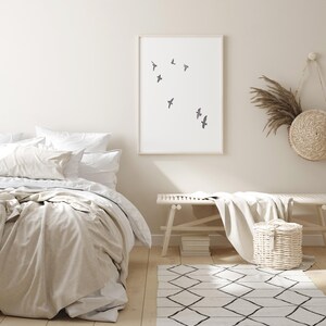 May include: A serene bedroom scene featuring a bed with white and beige bedding, a framed art print with flying birds, a wooden bench, and a woven basket. A geometric patterned rug and decorative wall hangings complete the calming aesthetic.