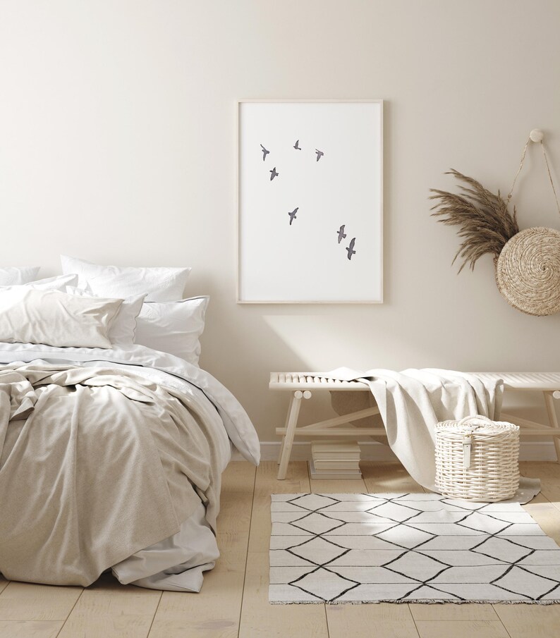 May include: A serene bedroom scene featuring a bed with white and beige bedding, a framed art print with flying birds, a wooden bench, and a woven basket. A geometric patterned rug and decorative wall hangings complete the calming aesthetic.