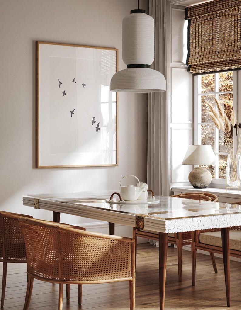 May include: A dining room scene featuring a rectangular table with a glass top and white trim. Wicker chairs surround the table. A framed artwork with bird silhouettes hangs on the wall. A white pendant light hangs above the table.