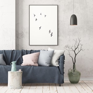 May include: A framed art print featuring a minimalist design of several birds in flight against a white background. The artwork hangs above a blue sofa with decorative pillows. A vase with branches and a hanging lamp complete the room's decor.