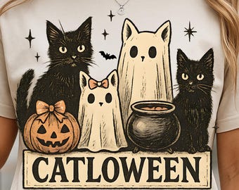 Op de afbeelding: Beige T-shirt met een Halloween-thema. Het ontwerp bevat zwarte katten, een pompoen, een ketel en spookfiguren. De tekst "CATLOWEEN" staat op een rechthoekige banner onder de illustraties.