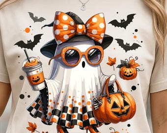 May include: Beige t-shirt featuring a cartoon ghost in a Halloween theme. The ghost wears a black witch hat, orange polka dot bow, and sunglasses. It holds a pumpkin-spiced drink and a pumpkin-shaped purse. Black bats and orange leaves are scattered around.
