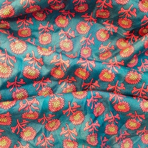 May include: Teal fabric with a repeating pattern of pink and yellow flowers. The fabric has a subtle sheen and a soft texture.