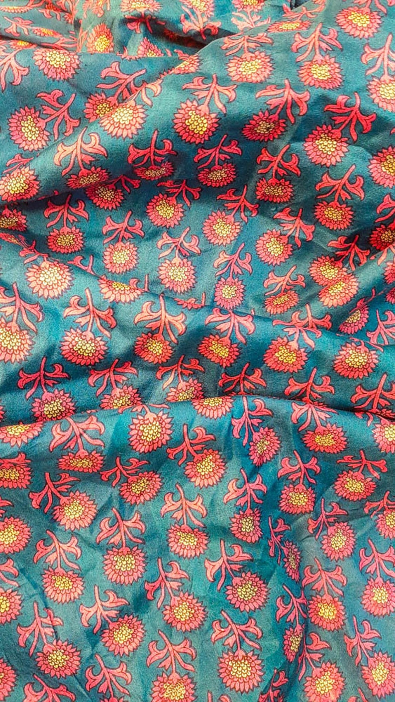 May include: Teal fabric with a repeating pattern of pink and yellow flowers. The fabric has a subtle sheen and a soft texture.
