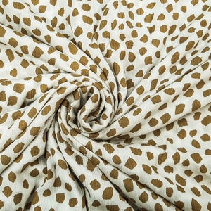 May include: Off-white fabric featuring a repeating pattern of brown, irregular spots. The material is arranged in a spiral, highlighting its texture and drape. Suitable for clothing or home furnishings.