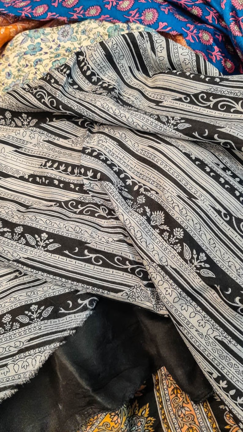 May include: A black and white patterned fabric with a repeating design of stripes and floral motifs. The fabric is folded and draped, showing the texture and detail of the pattern.