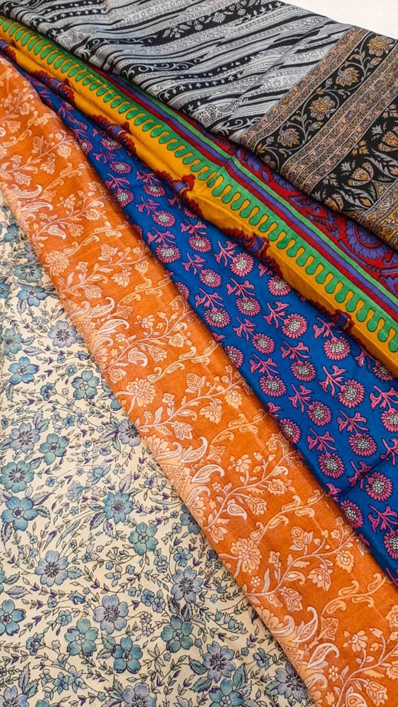 May include: A stack of colorful fabric with floral patterns. The fabric is in shades of blue, orange, yellow, and green. The fabric is arranged in a layered pattern, with the top layer being a black and white striped fabric.