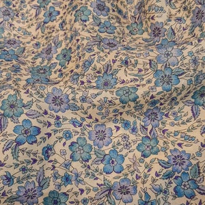 May include: A white fabric with a blue and purple floral pattern. The fabric is soft and has a subtle sheen.