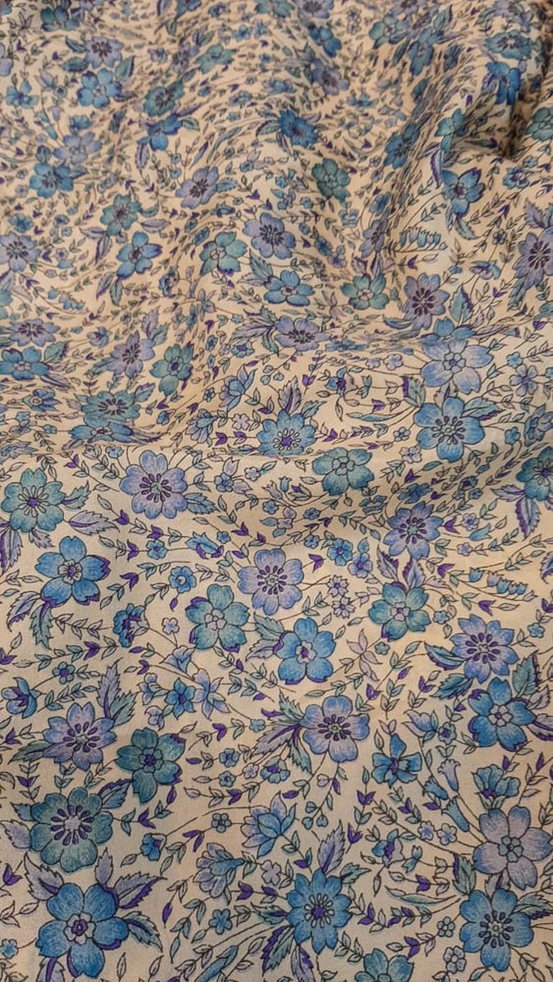 May include: A white fabric with a blue and purple floral pattern. The fabric is soft and has a subtle sheen.
