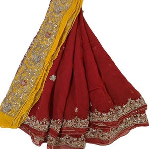 Könnte beinhalten: Ein drapiertes rotes Textil mit aufwendigen Stickereien und Verzierungen. Der Rand weist detaillierte Gold- und Silberfäden auf, mit einem leuchtend gelben Akzent. Der Stoff ist gefaltet und zeigt das verzierte Design und die Textur.