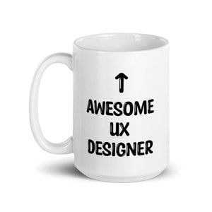 K&ouml;nnte beinhalten: Wei&szlig;e Keramik-Kaffeetasse mit einem schwarzen Pfeil, der nach oben zeigt, und dem aufgedruckten Text "AWESOME UX DESIGNER".