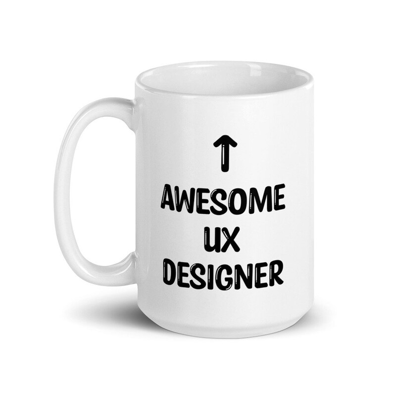 K&ouml;nnte beinhalten: Wei&szlig;e Keramik-Kaffeetasse mit einem schwarzen Pfeil, der nach oben zeigt, und dem aufgedruckten Text "AWESOME UX DESIGNER".