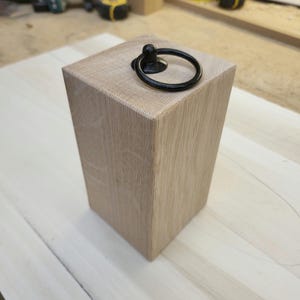 May include: A light wood doorstop with a black metal ring handle.