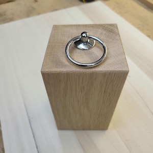 May include: A wooden doorstop with a chrome ring handle. The doorstop is made of light brown wood and has a smooth finish.