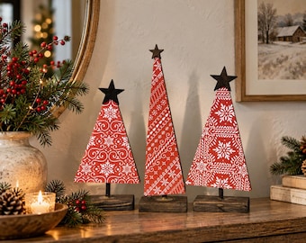 May include: Three triangular wooden Christmas tree decorations in varying heights, each featuring a vibrant red surface with white snowflake and scroll patterns, topped with a dark brown star and mounted on a rectangular wooden base.