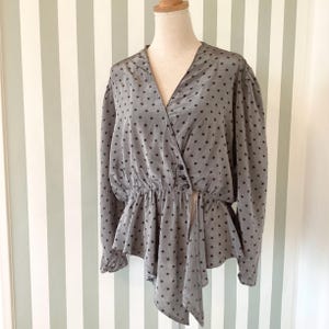 May include: Gray wrap top with black star pattern. The top features a V-neck, long sleeves, and a peplum-style hem. It has a button closure and a draped asymmetrical design.
