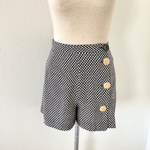 Puede incluir: Pantalones cortos de color negro y blanco con estampado, cintura alta y tres botones grandes de color beige en el lateral.